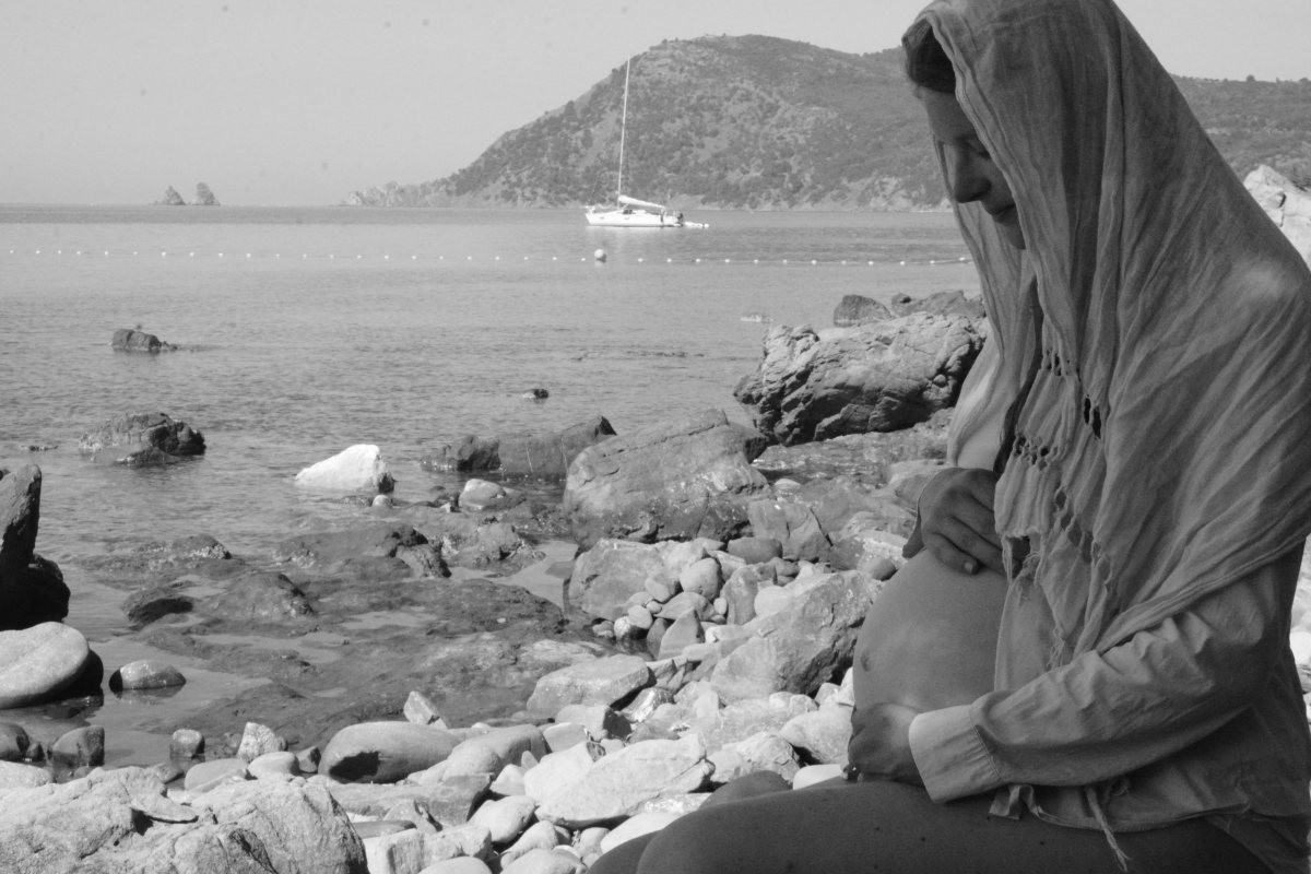 Veiled expectant mother contemplating her belly by the sea, sacred pregnancy in black and white